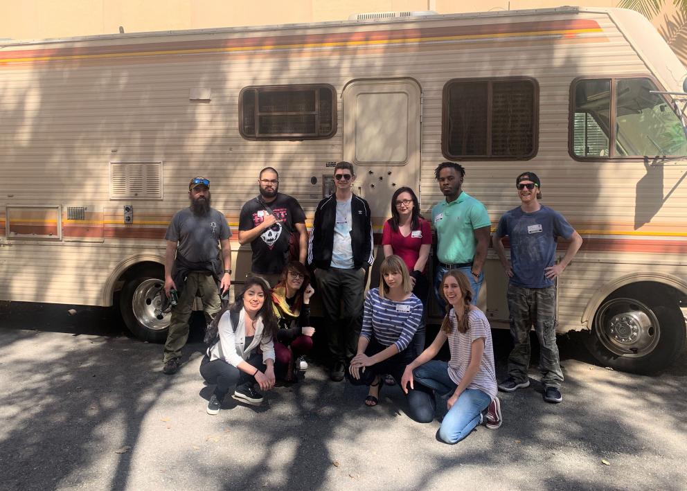 A small group of students pose in front of an RV with fake bullet holes in the door.