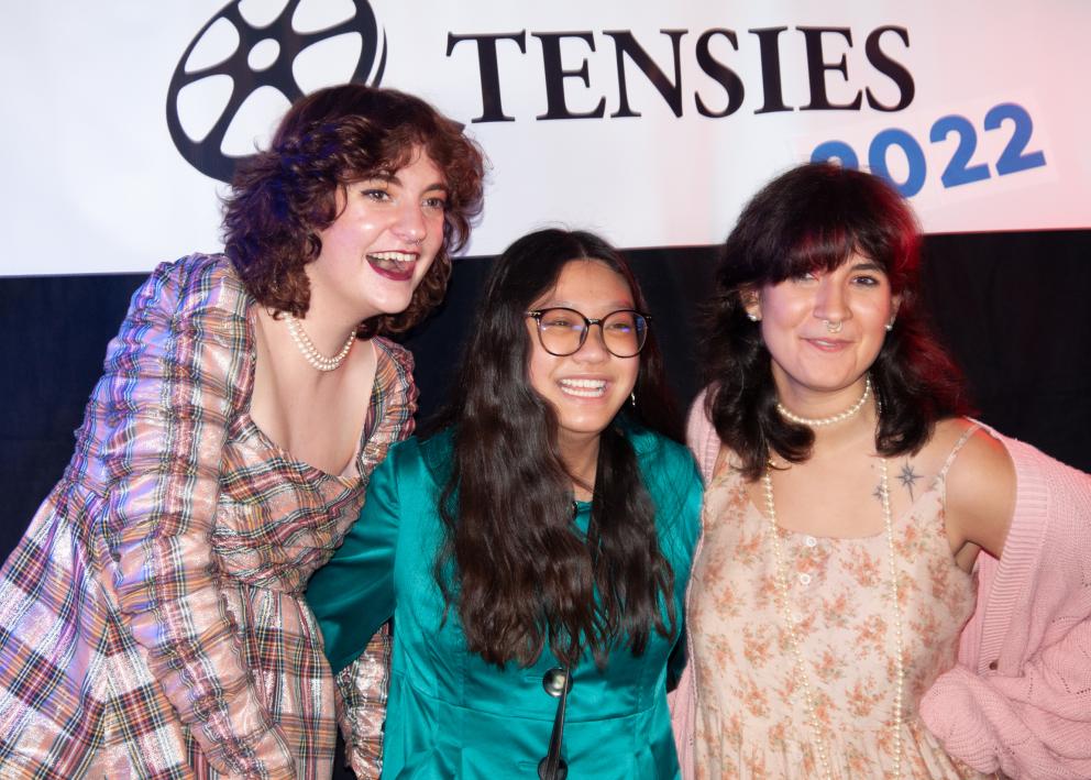 Three women smile while standing in front of a Tensies 2022 banner.