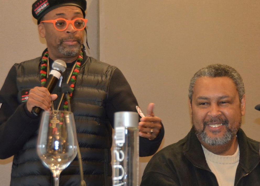 A man with a microphone stands next to another man.