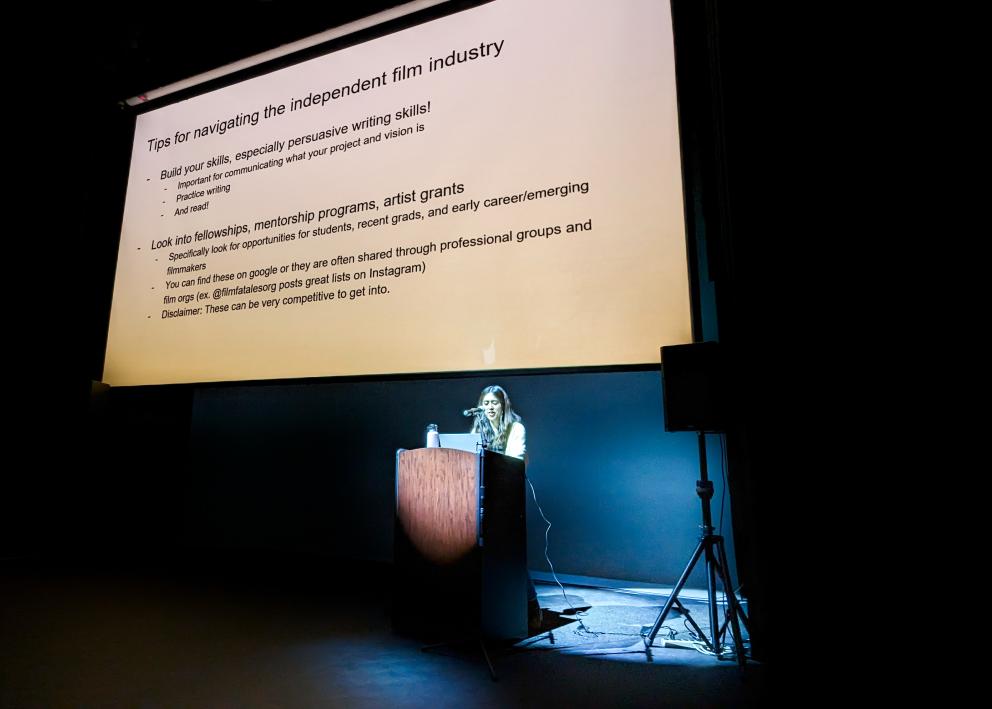 A woman at a podium stands below a screen with tips on navigating the independent film industry.