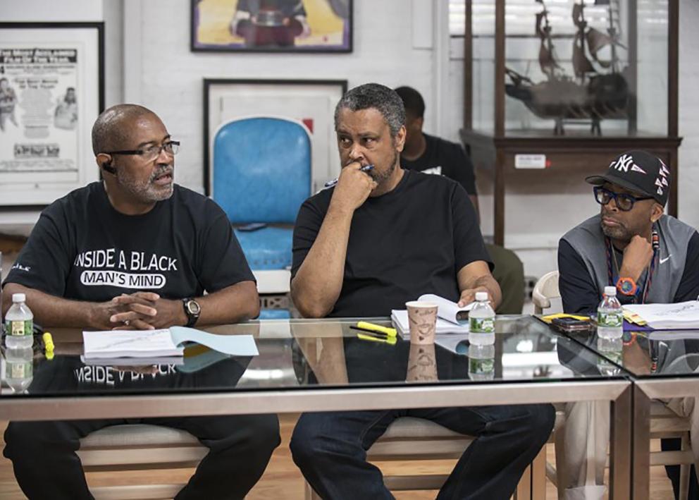 Three men sit at a table in discussion.