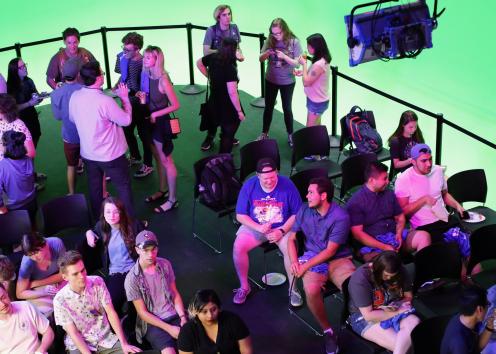 A crowd of students socialize on a soundstage next to a green screen cyclorama.
