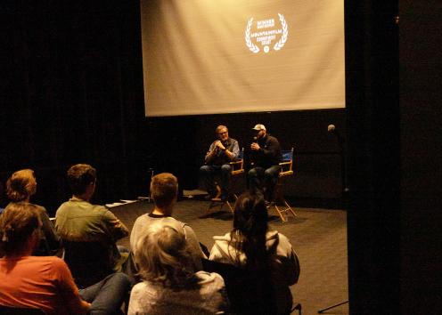Two men on directors chairs speak to an audience.