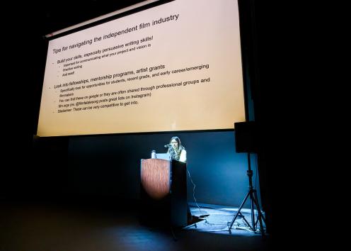 A woman at a podium stands below a screen with tips on navigating the independent film industry.