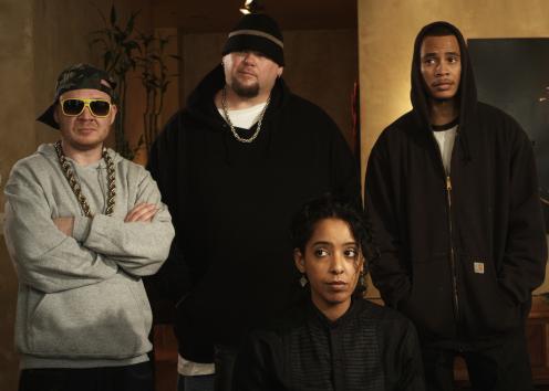 Three men dressed as rappers stand next to an actress.